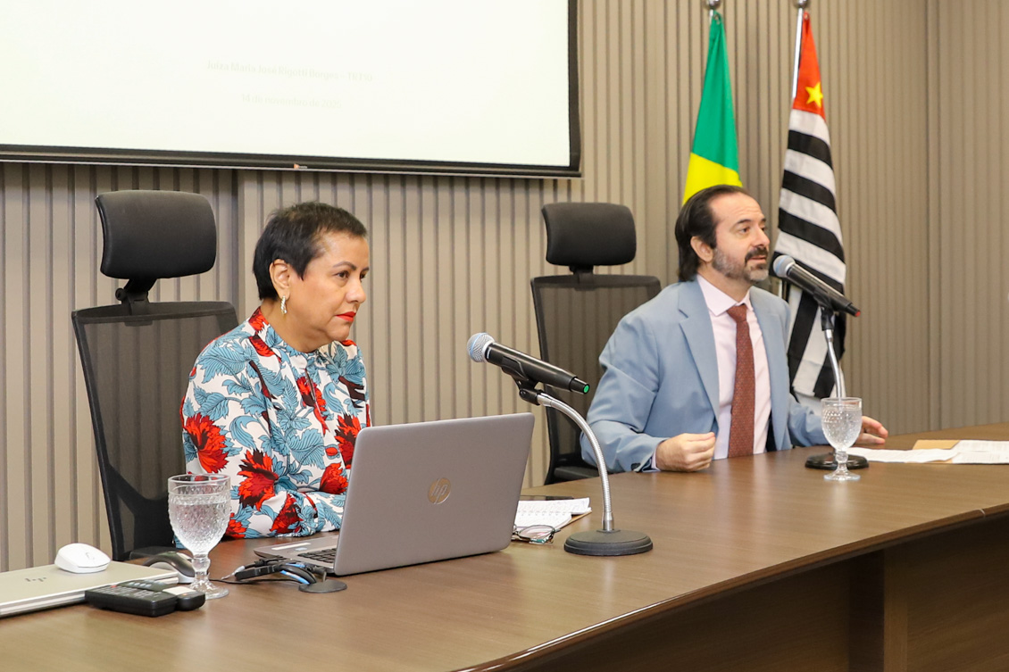 "Dra. Maria José e Dr. Rodrigo estão na mesa alta, diante de microfones"