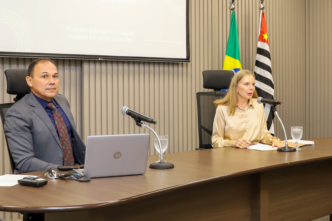 "Auditor Evandro e Dra. Maria da Graça na mesa alta diante de microfones"