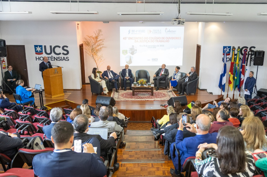 "Abertura do evento, com autoridades em cadeiras no palco, e plateia assistindo no auditório"
