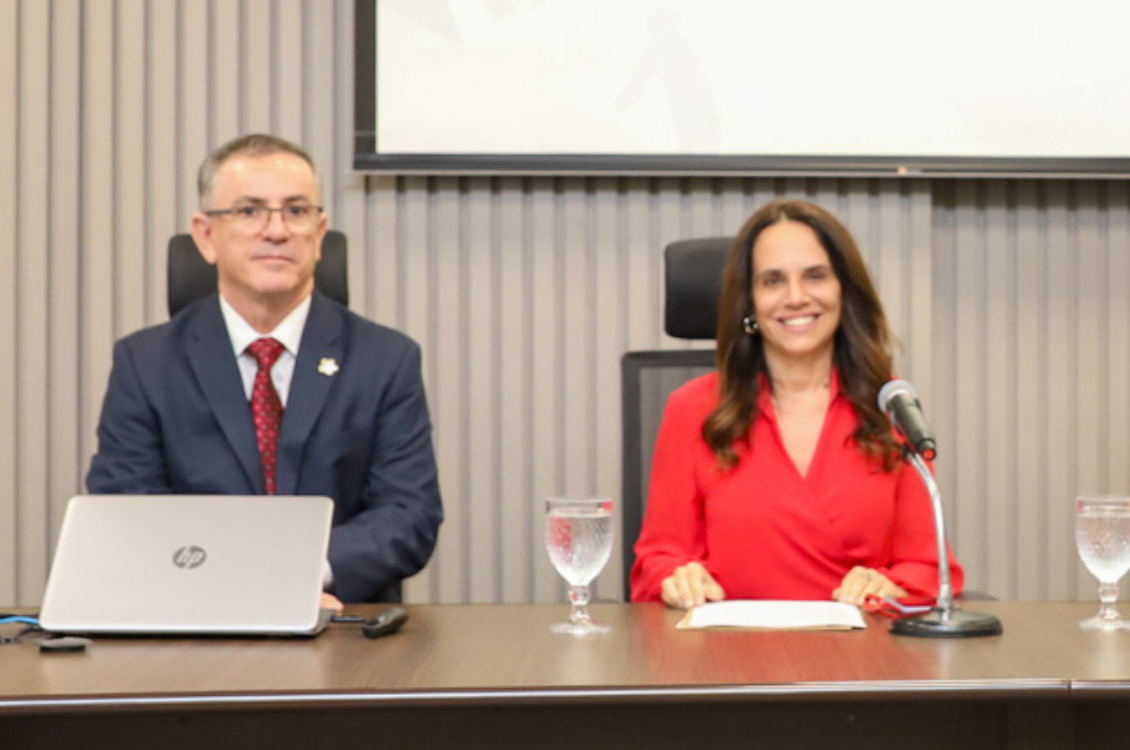 "Dr. João Batista está sentado à mesa alta, ao lado da Dra. Adriene"