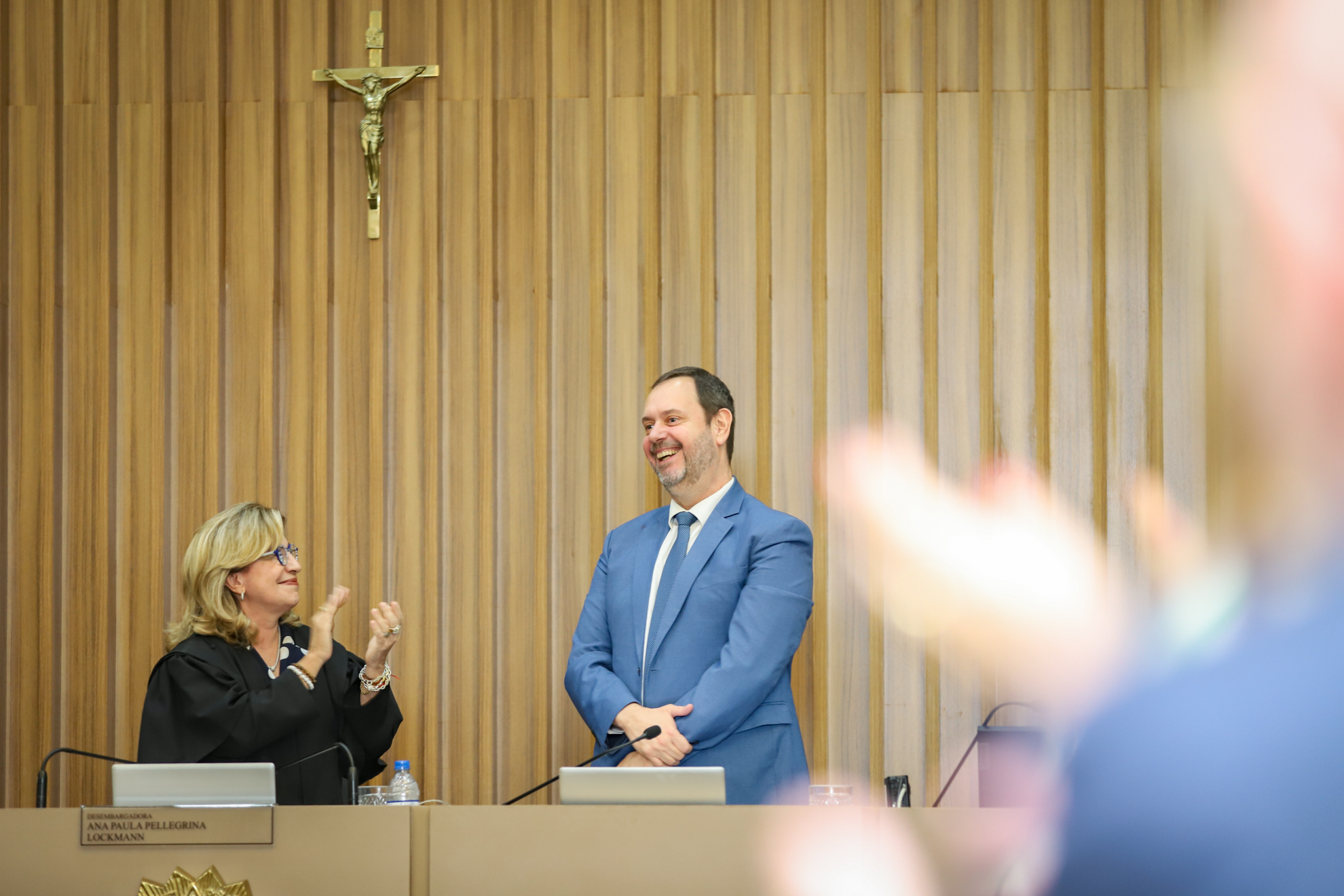 "Foto da Dra. Ana Paula aplaudindo Paulo Almeida, ambos de pé na mesa alta da sessão"