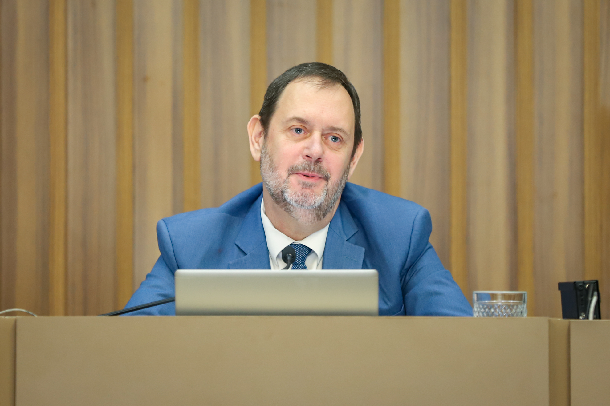 "Foto de Paulo Almeida sentado à mesa alta, falando ao microfone em frente a um notebook de cor prata"