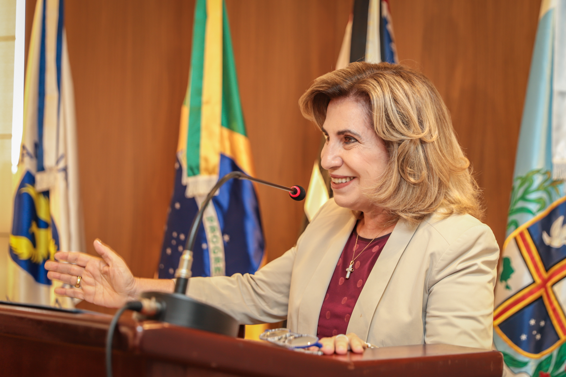"Dra. Ana Paula sorri ao falar ao microfone no púlpito"