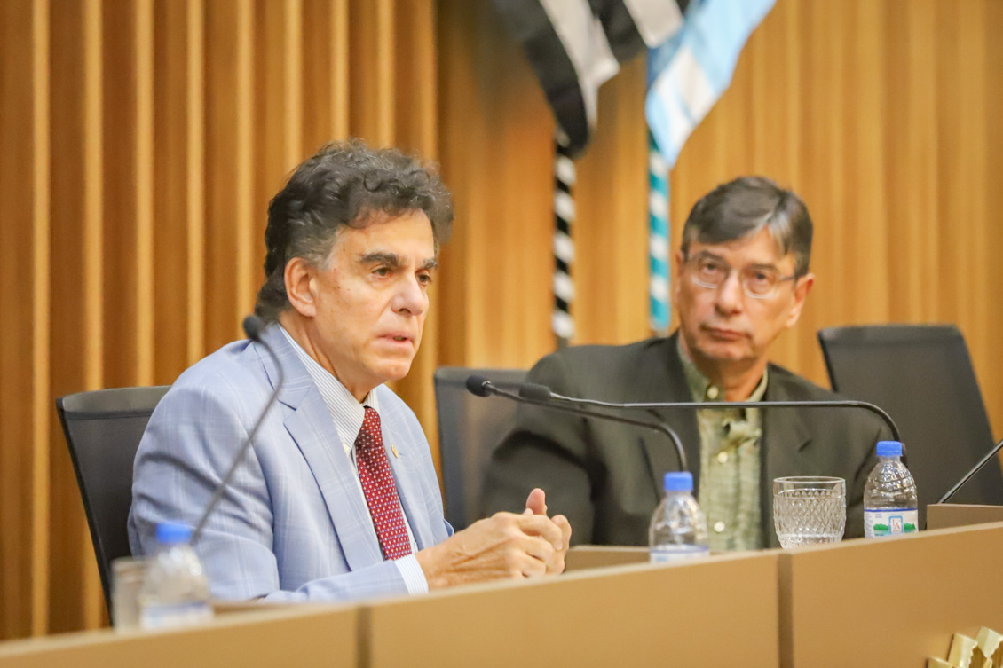 "Ministro Vieira de Mello fala ao microfone na mesa alta, ao lado de Marcio Pochmann"