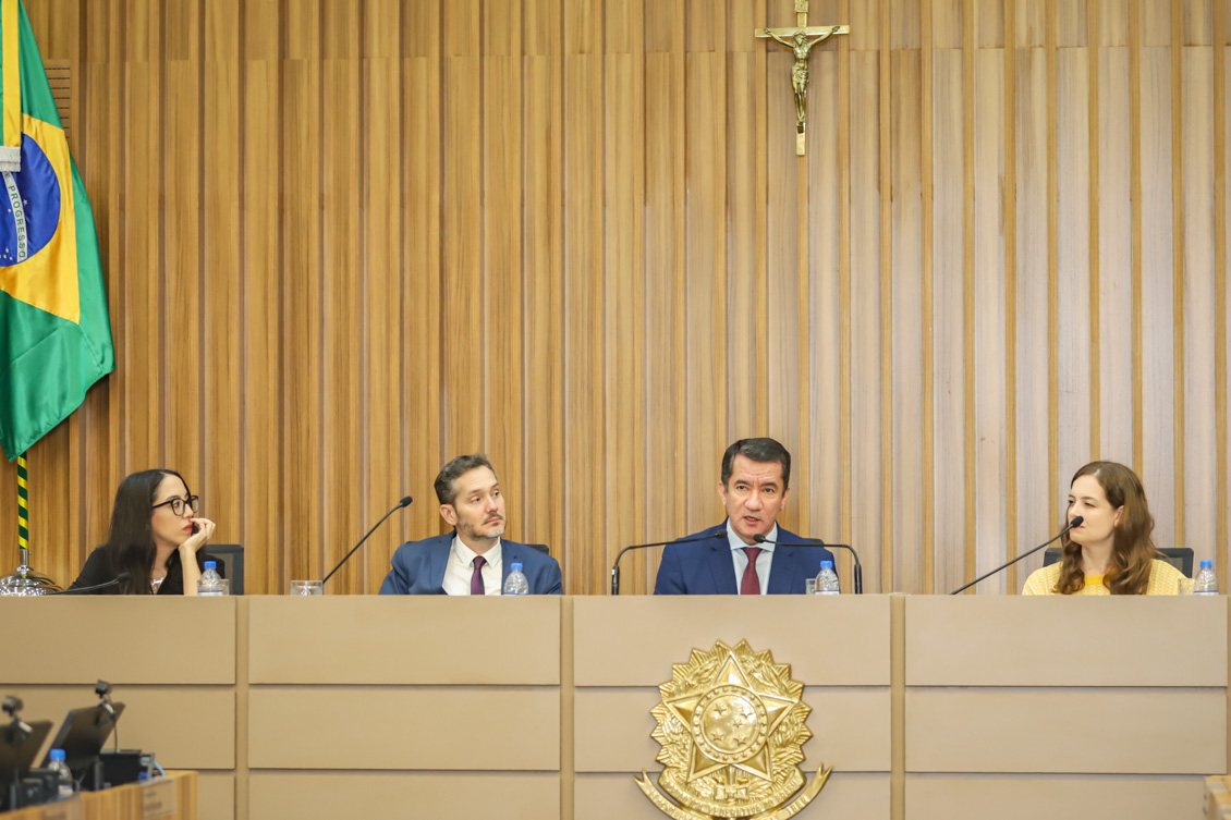 "Desembargador comanda painel ao lado de três palestrantes, duas mulheres e um homem"