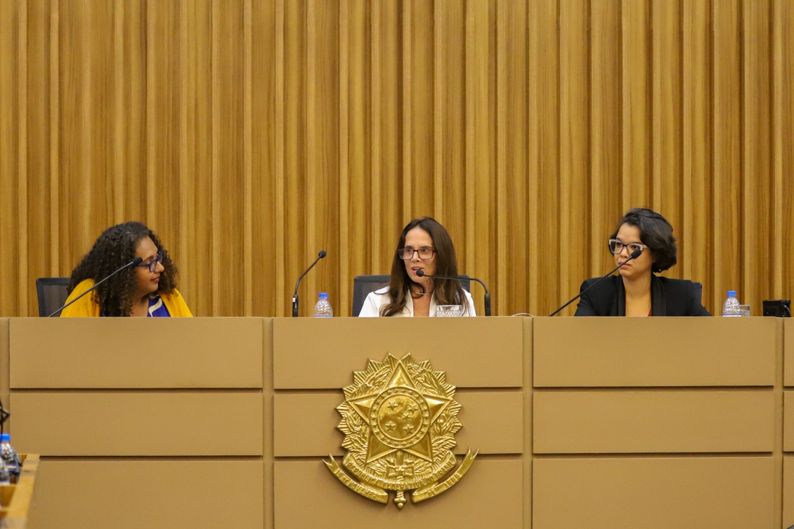 "Desembargadora Adriene comanda painel na mesa alta, ladeada pelas palestrantes"