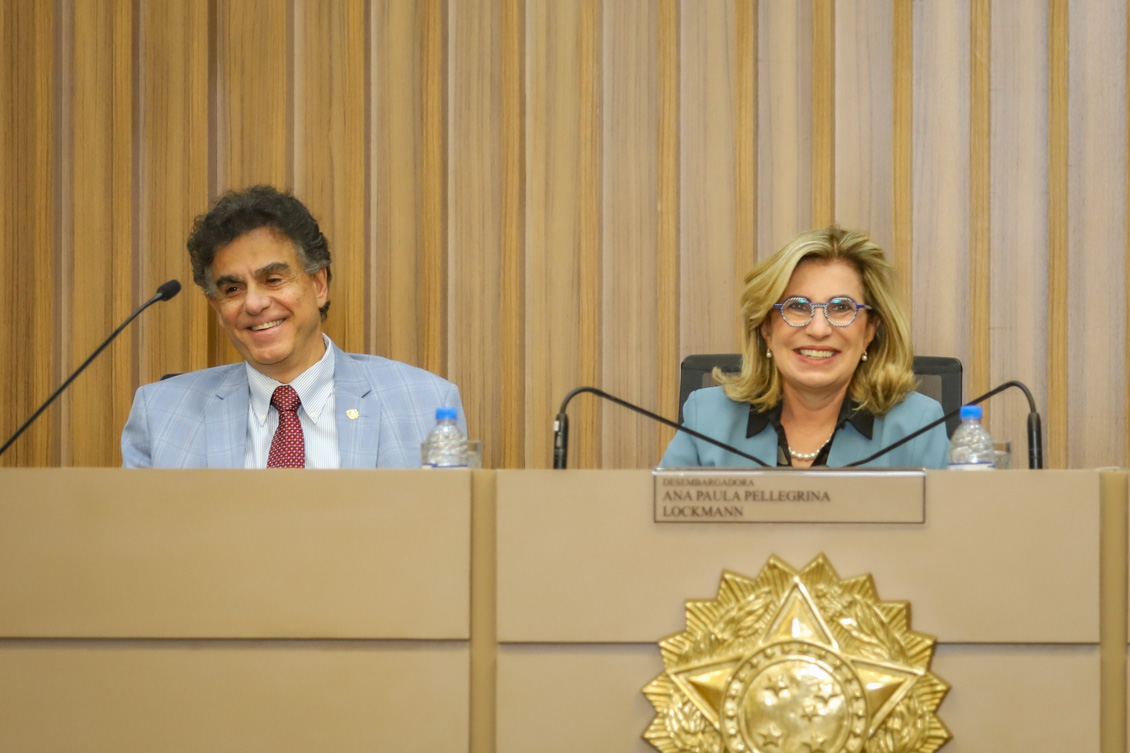 "Ministro Vieira de Mello e Dra. Ana Paula sorriem, sentados à mesa alta"