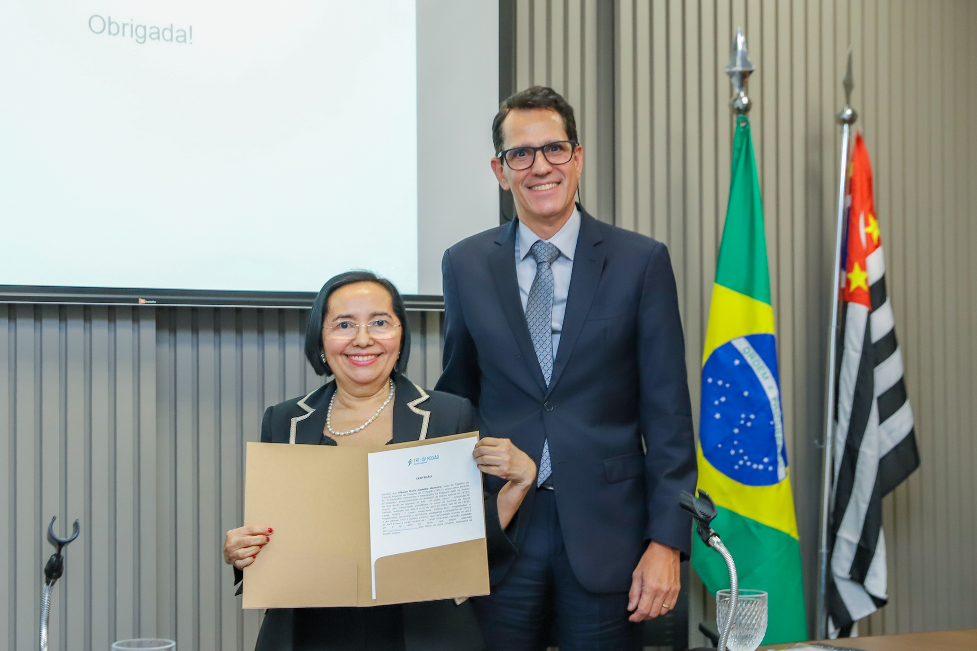 "Dra. Glaucia segura o certificado ao lado do Dr. Alessandro em foto posada"