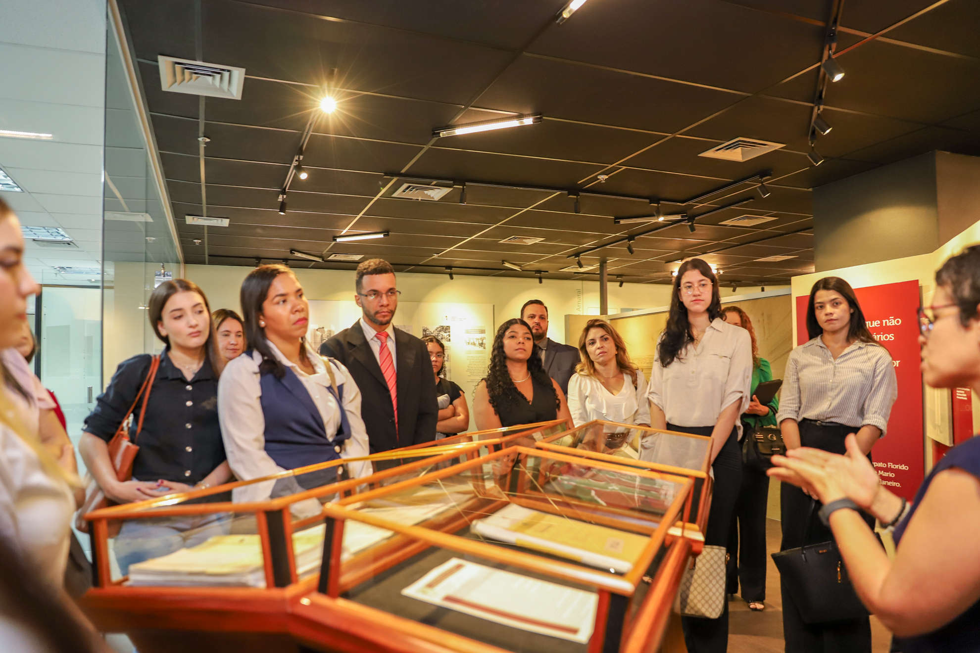 "Estudantes estão em pé, no Centro de Memória, ouvindo as explicações da historiadora Flávia"