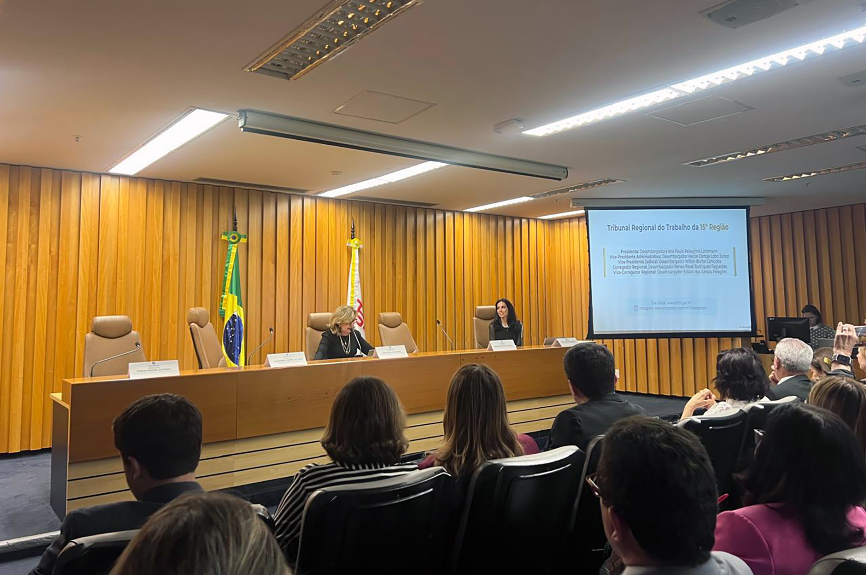 "Dra. Ana Paula e Renata na mesa de trabalhos, com público de costas em primeiro plano"