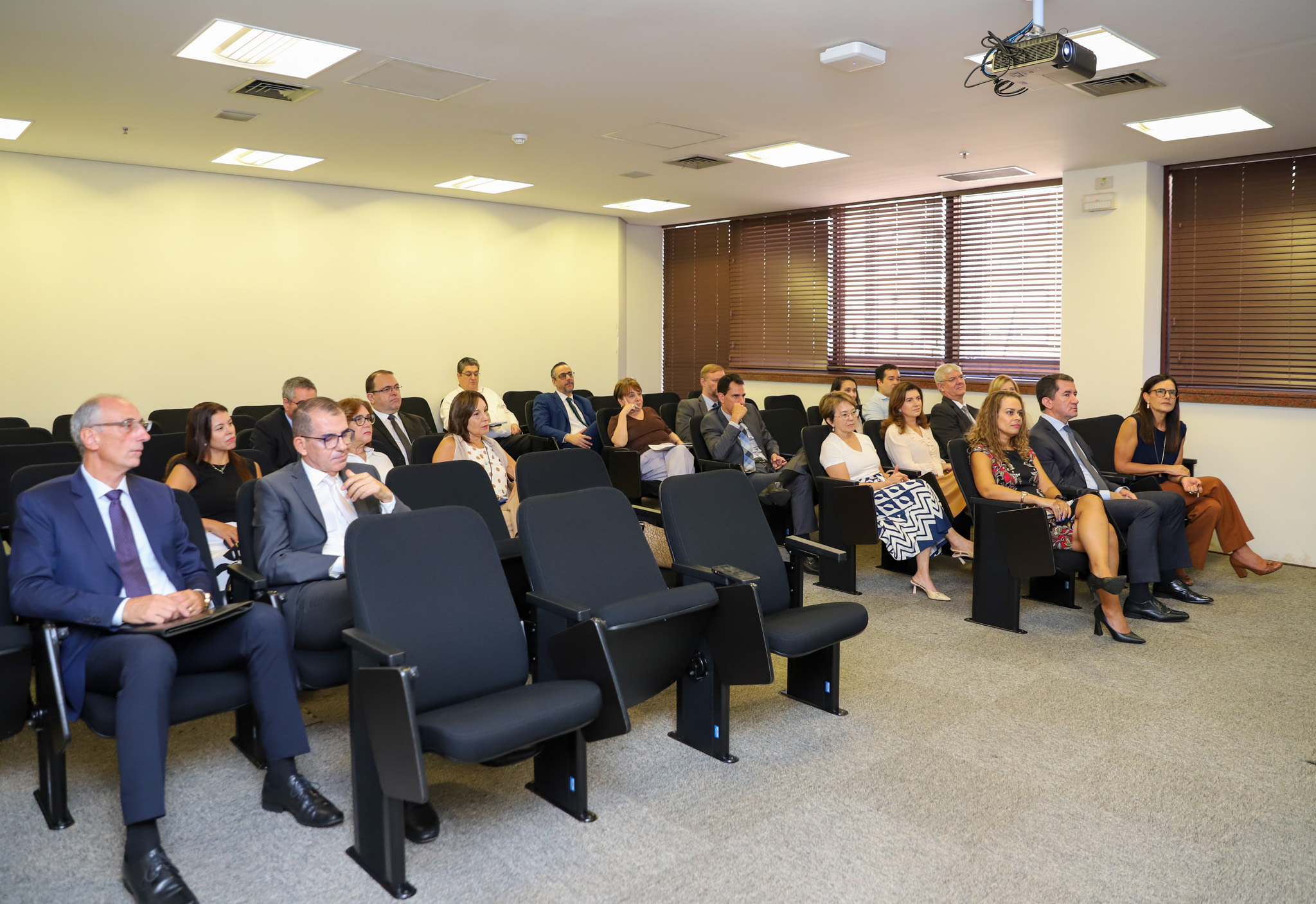 "várias pessoas sentadas em cadeiras pretas em um pequeno auditório"