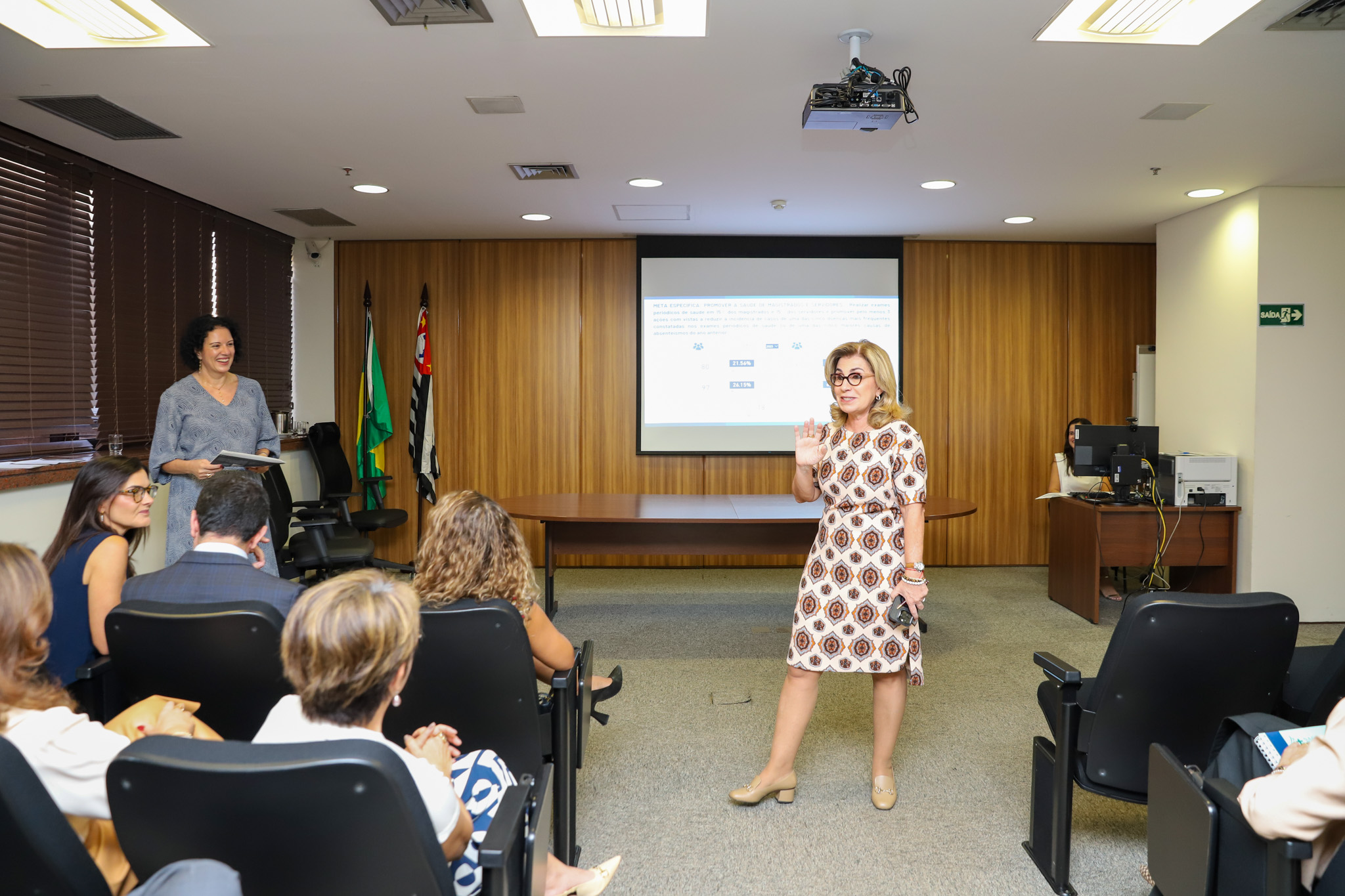 "Dra. Ana Paula está de pé interagindo com as pessoas sentadas nas cadeiras do auditório"