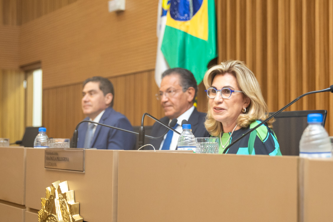 "Dra. Ana Paula sorri na mesa alta ao lado do ministro e de seu juiz auxiliar"