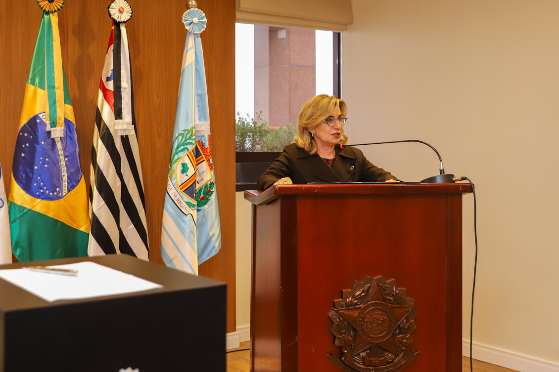 "A presidente Ana Paula fala ao microfone, no púlpito"