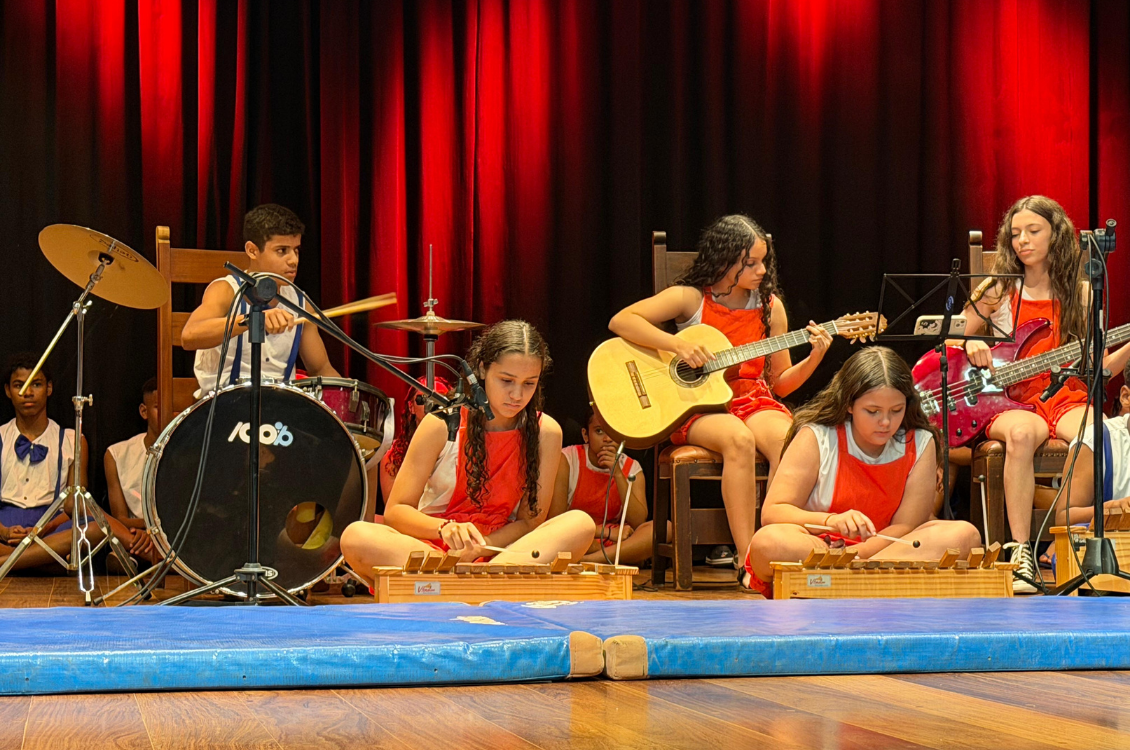 "crianças tocam instrumentos no palco, vestidas de vermelho"