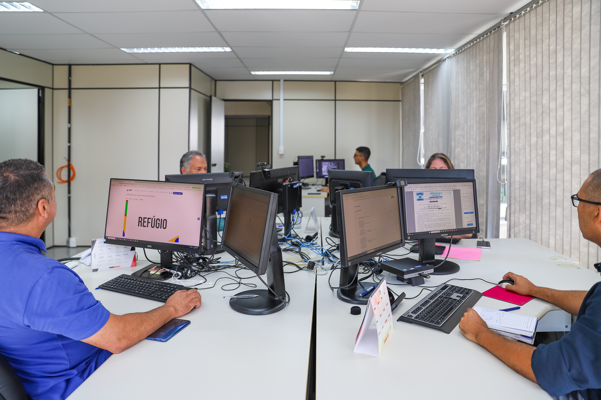 "Quatro funcionários do setor atuam em seus computadores dispostos em quatro ilhas"