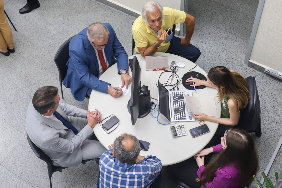 "Foto de uma audiência de conciliação em mesa redonda, com servidora e partes"