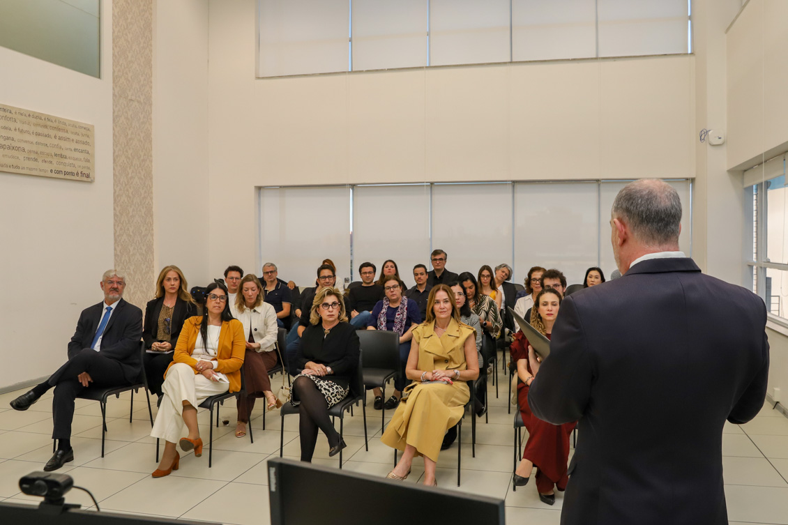 "Um homem branco fala ao microfone, sendo observado por diversas autoridades que estão sentadas"