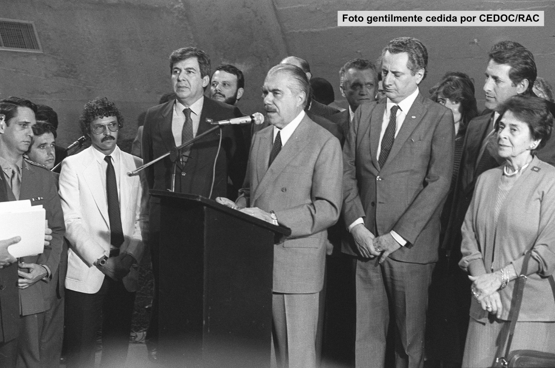 "Foto em preto e branco de José Sarney no púlpito e ao microfone, com diversas autoridades durante a sanção da Lei no Centro de Convivência"