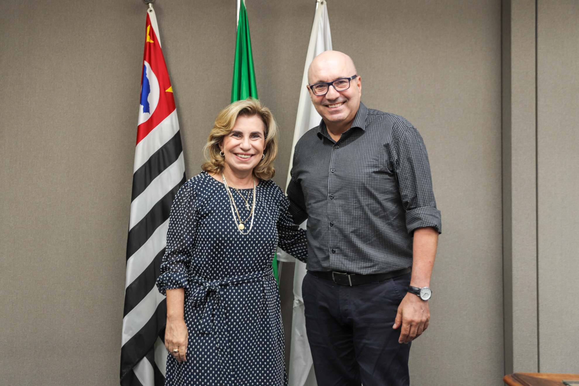 ""Dra. Ana Paula está de pé ao lado do prefeito de Campinas, Dário Saad, em frente as bandeiras de SP, Brasil e Campinas"
