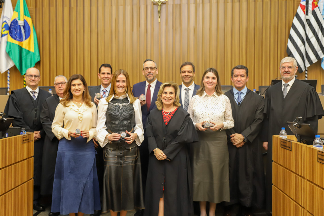 "Foto posada dos membros da alta administração ao lado dos juízes auxiliares que seguram a moeda. Todos de pé"