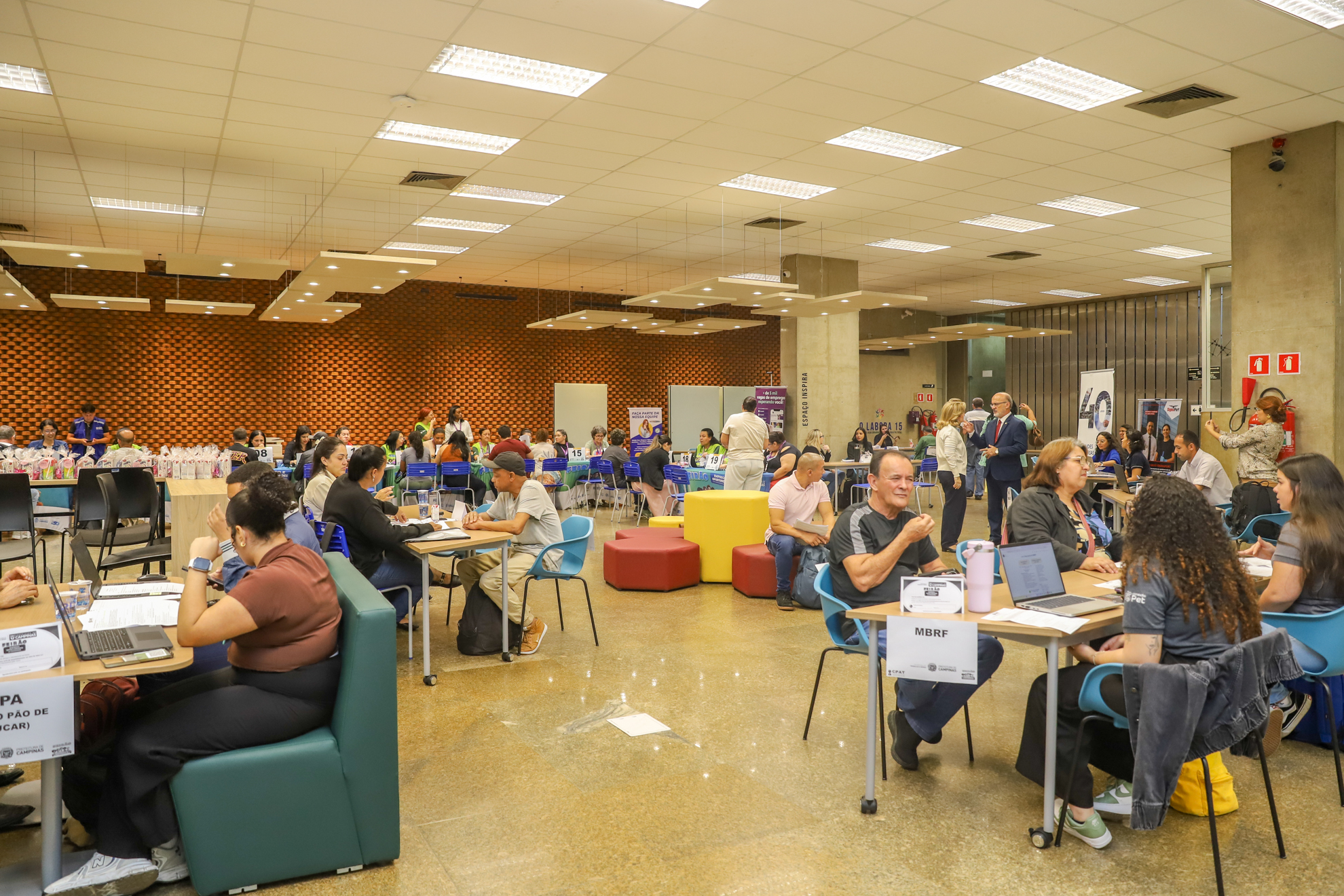 "foto geral do espaço com muitas pessoas sendo atendidas em mesas"