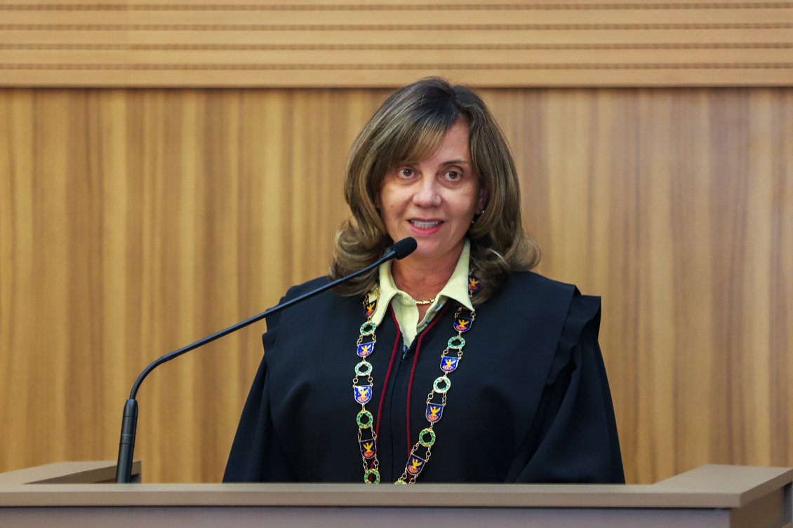 "Dra. Alvamari, de toga e colar, fala ao microfone no púlpito"