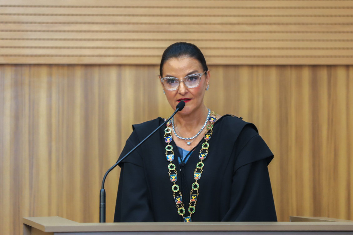 "Dra. Juliana, de toga e colar, fala ao microfone no púlpito"