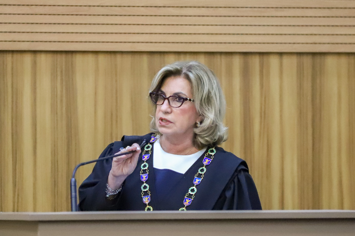 "Dra. Ana Paula, de toga e colar, fala ao microfone no púlpito"