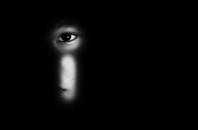 foto em preto e branco exibe uma criança olhando pela fechadura