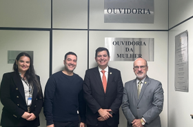 foto posada do ouvidor, de sua assessora, do Dr. Edmundo e de Alan, com as placas Ouvidoria e Ouvidoria da Mulher ao fundo