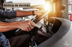 mãos masculinas em volante de caminhão, ao fundo outros caminhões.