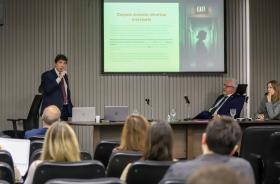 imagem geral do auditório com os palestrantes ao fundo e o público presente em primeiro plano. No telão, o tema da palestra