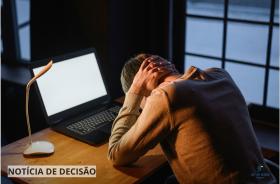 homem está cabisbaixo, com as mãos cruzadas no pescoço, em frente a um notebook
