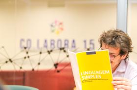 servidor segura cartilha de capa amarela sobre linguagem simples no ambiente do Co.Labora 15
