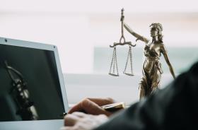 homem dedilha notebook com a imagem da justiça ao fundo