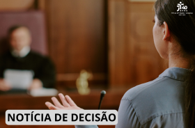 Mulher fala ao microfone em um ambiente de tribunal, com o magistrado desfocado ao fundo.