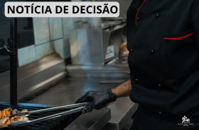 A imagem mostra um profissional da cozinha, usando uniforme e luvas, preparando alimentos em uma churrasqueira industrial.