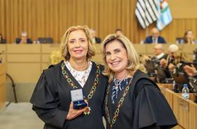 Dra. Tereza posa para foto segurando a medalha, ao lado da Dra. Ana Paula 