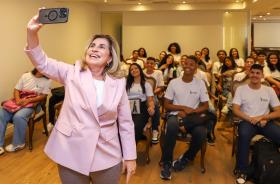 Dra. Ana Paula tira selfie com os aprendizes que estão sentados nas cadeiras do salão nobre