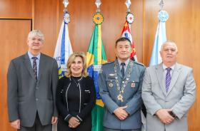 Homenageado possa para foto ao lado dos desembargadores Edison Pelegrini, Ana Paula e Helcio Dantas em frente a uma parede de madeira e quatro bandeiras
