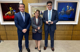 Dr. Renan, Dra. Ana Paula e ministro Vieira de Mello segurando a caixa com a medalha. Todos de pé, com quadros ao fundo