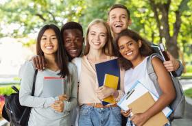 cinco estudantes sorridentes, de várias etnias, segurando livros e cadernos em um local aberto, com árvores