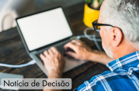 A foto mostra um trabalhador na faixa dos 65 anos de idade trabalhando num computador