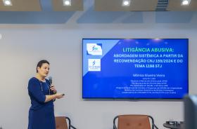 juíza Mônica fala ao microfone de pé, apontando para uma tela com dados sobre o tema