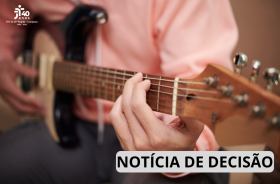 Um homem toca um violão, o foco está na sua mão. 
