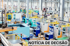Fotografia de uma área industrial, com diversas máquinas e equipamentos de produção distribuídos pelo amplo espaço. Há estruturas metálicas, tubulações, cabos, esteiras, painéis e equipamentos de proteção em cores predominantemente azul, verde, amarelo, branco e laranja. Ao fundo, observam-se outras máquinas e linhas de produção. Na parte inferior direita, há uma faixa branca com a inscrição “NOTÍCIA DE DECISÃO”