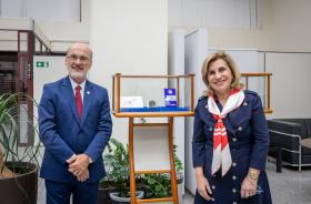 Um homem e uma mulher posam para a foto ao lado de uma caixa onde estão em exposição um selo e uma moeda comemorativa dos 40 anos do TRT 15.