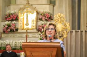Dra. Ana Paula está no púlpito fazendo a leitura da Carta. Ao fundo, o nicho de Nossa Senhora Aparecida