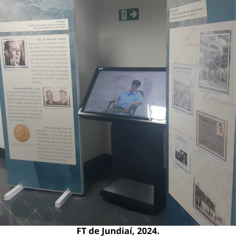 Uma tela com painel de vídeo e dois painéis com textos e imagens nas cores verde e bege. Atrás dos painéis, há uma parede na cor bege.